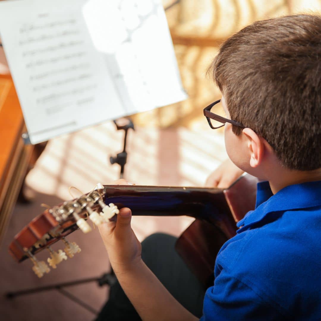 A young boy playing guitar and reading sheet music.